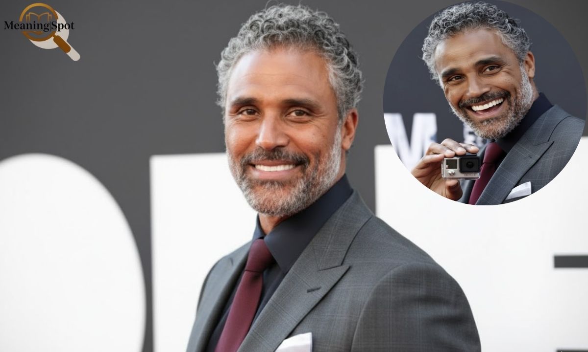 A well-dressed man in a gray suit smiling confidently at an event, representing a professional look often used in articles discussing success and topics like Rick Fox Net Worth.